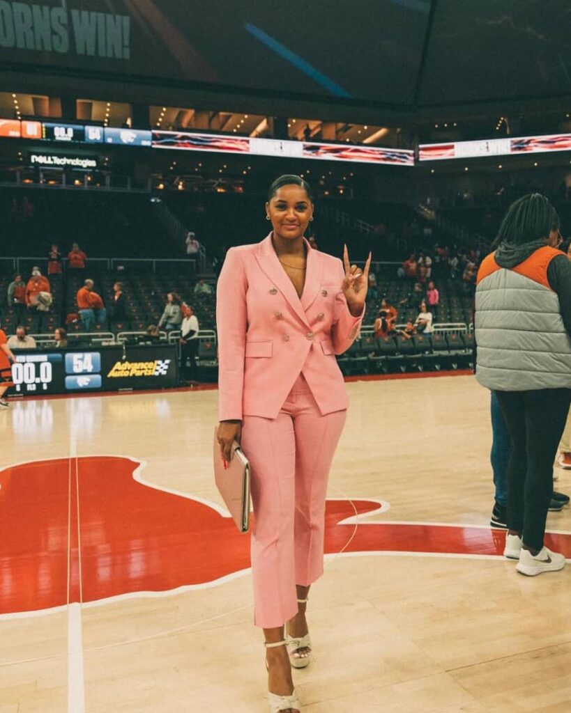 Sydney slaying a peach coloured pant suit and jacket gesturing the love sign with her fingers 
Credit:- Sydney Carter|Instagram