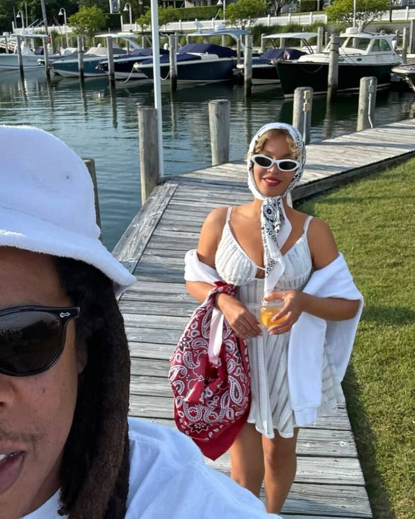 Jay Z features in a selfie alongside Beyonce who is holding a glass. Beyonce is dressed in a short white flare gown which she paired with z white bandana and shades.