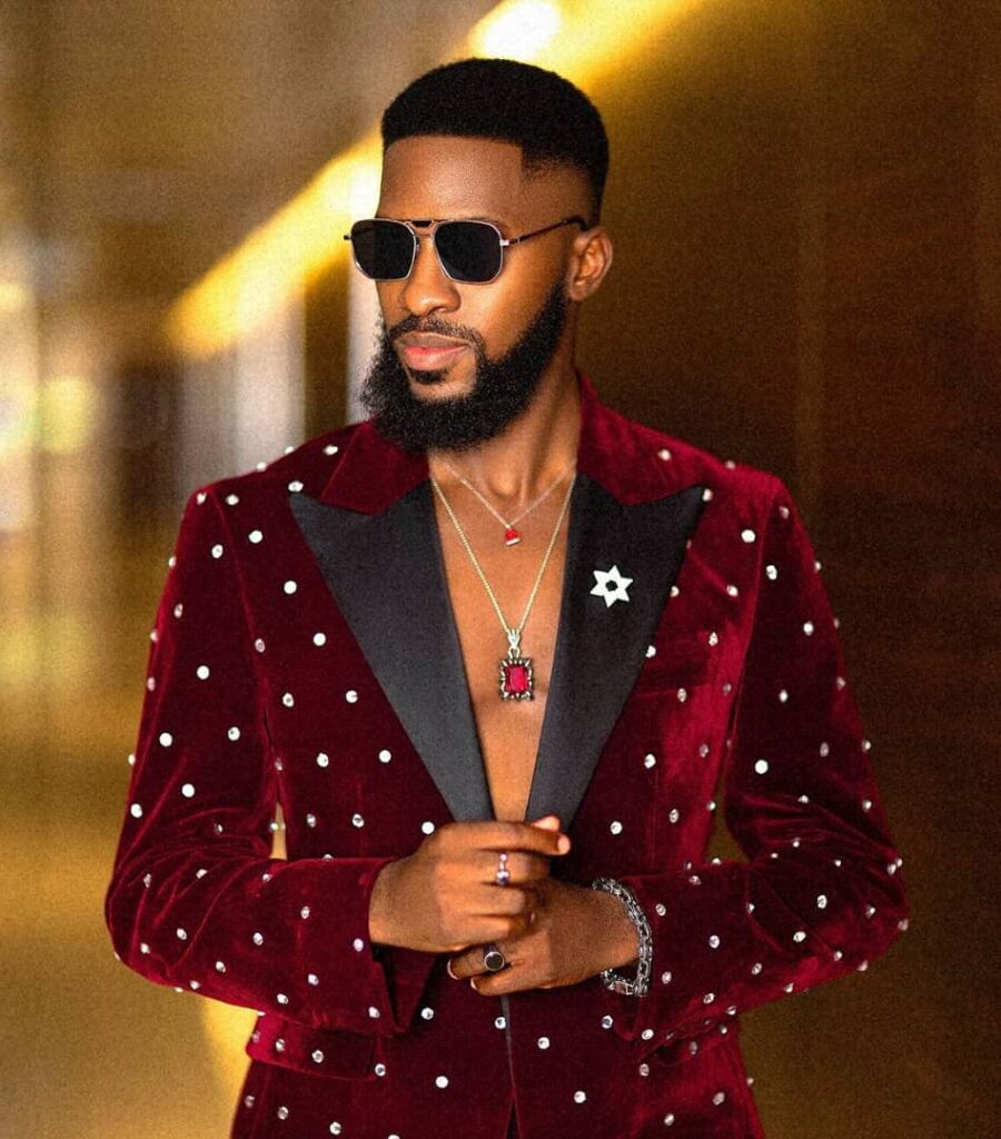 A headshot of Akin Faminu wearing a red velvet tuxedo